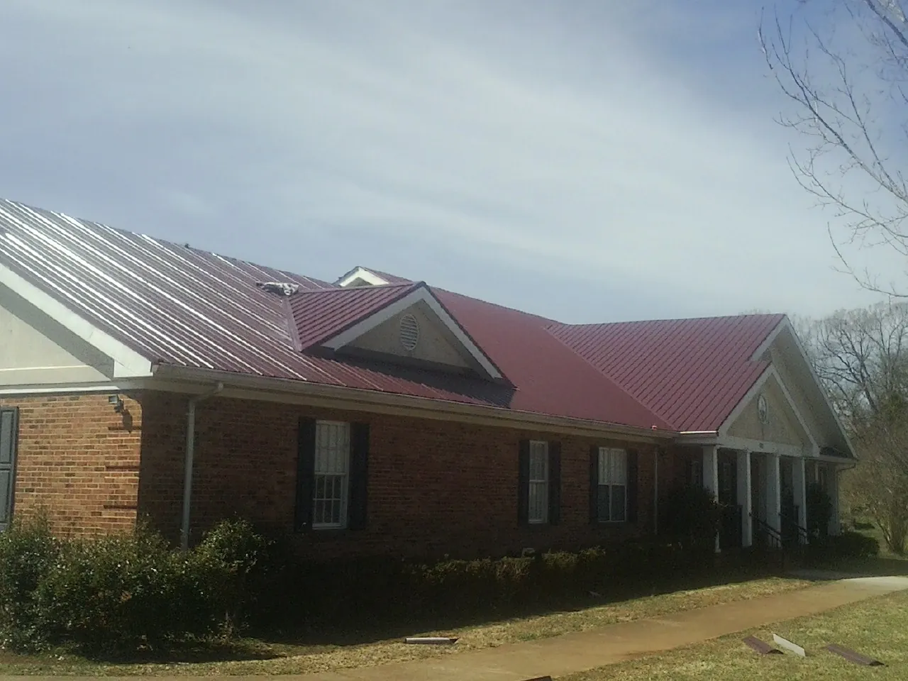 Red metal roof with gabled entries on a long brick building, from a Hail Damage Roof Repair job in Wharton